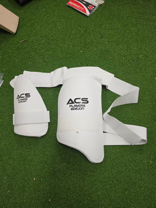 Flat lay view of white ACS Superlite Cricket Double Thigh Pads for left hand batsmen on a green turf surface from Albertacricketstore.com.