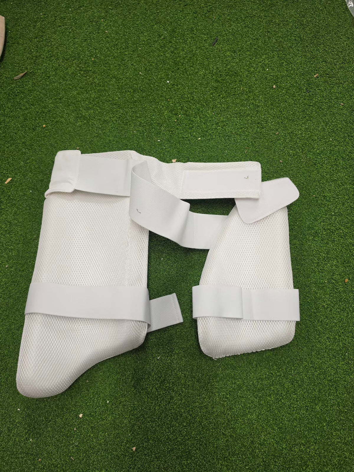 Overhead view of a complete SS cricket protective gear kit on green turf from Albertacricketstore.com, including blue batting pads, thigh guards, gloves, helmet, and a camo duffle bag