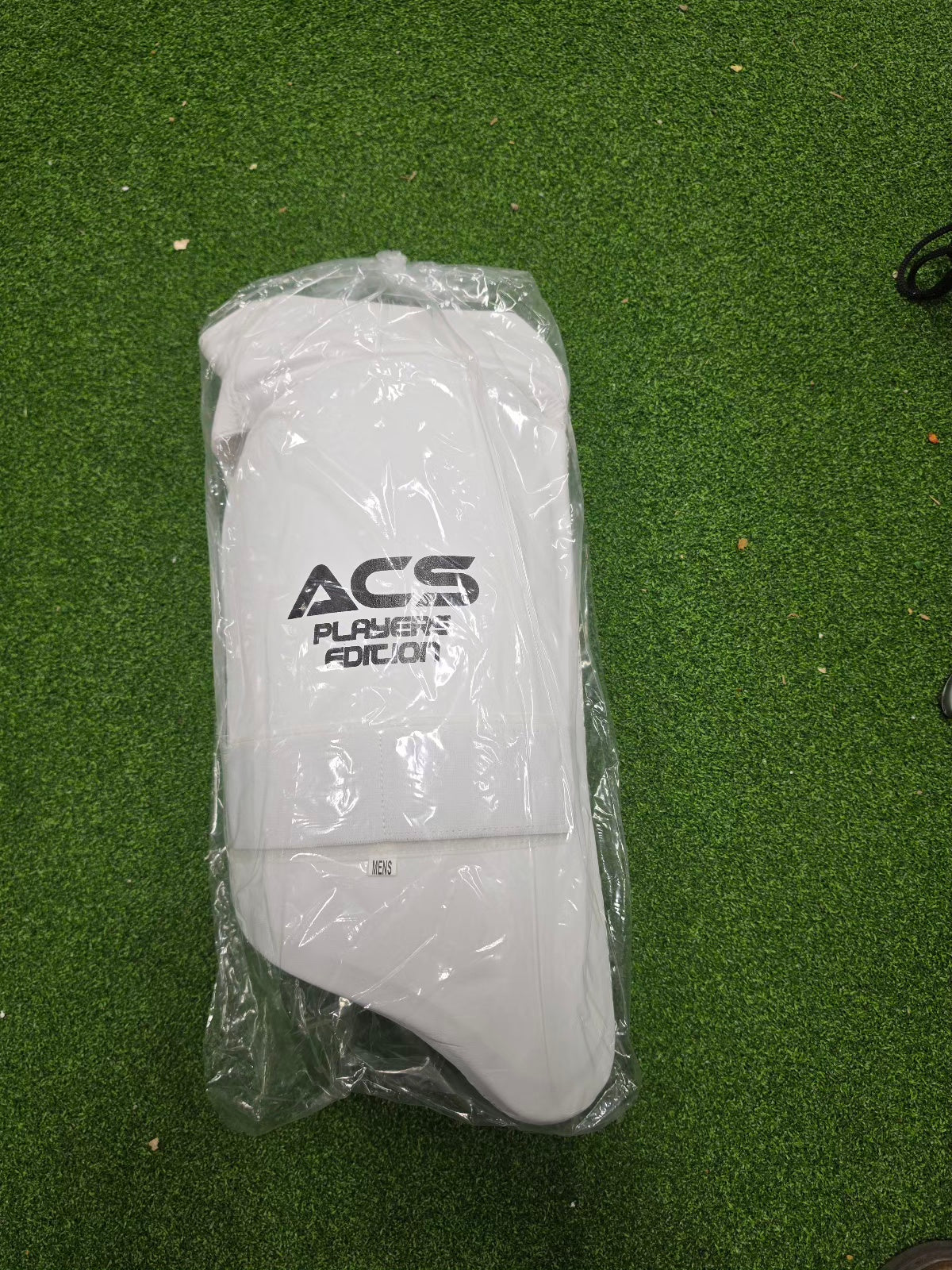 Overhead product arrangement of premium SS cricket gear from Albertacricketstore.com, including a camo duffle bag, navy blue batting pads, a navy helmet, and white guards.