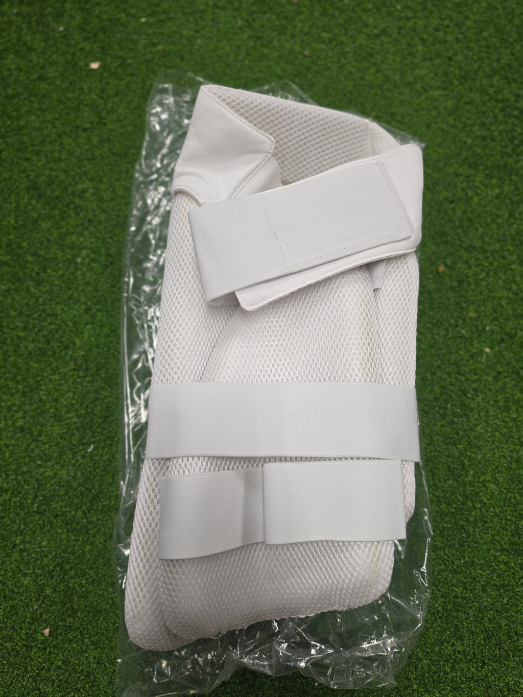 Front view of an ACS Players Edition white cricket thigh pad sealed in clear plastic wrap on green turf from Albertacricketstore.com.