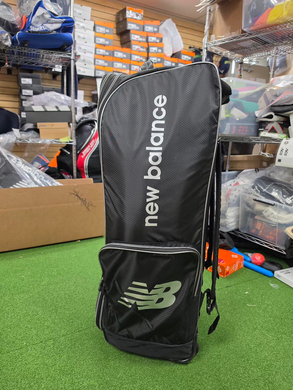 Black New Balance 10i combo duffle wheelie cricket kit bag standing upright in a sports gear store.