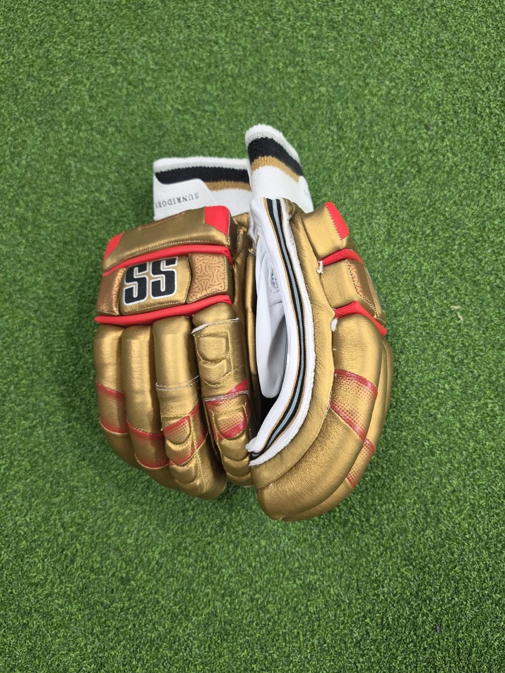 Close up top view of gold, red, and white SS Super Test Royal Challengers Bangalore IPL cricket batting gloves on artificial turf