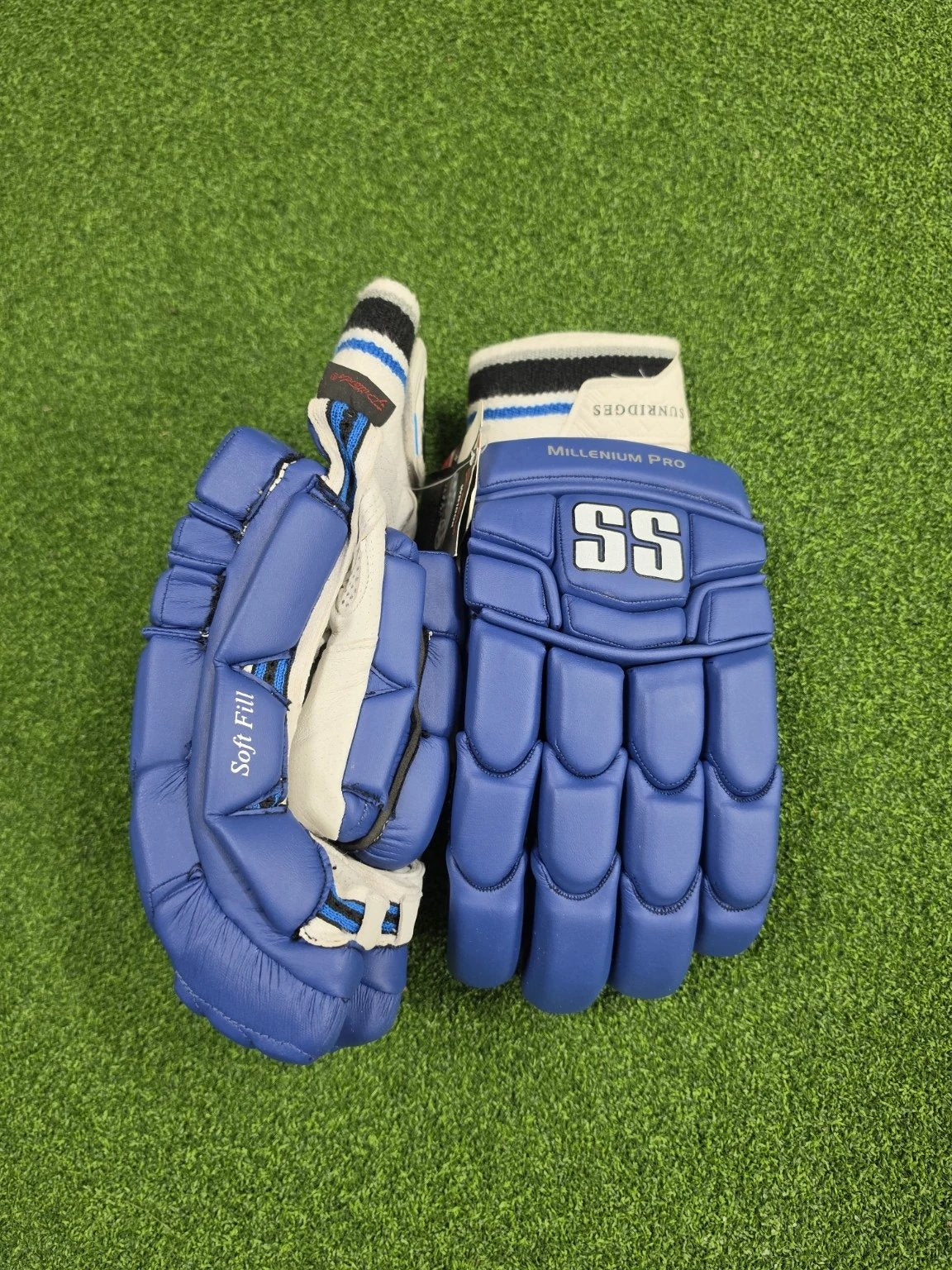 Side profile view of blue and white SS TON Millennium Pro adult cricket batting gloves on artificial turf showing side padding