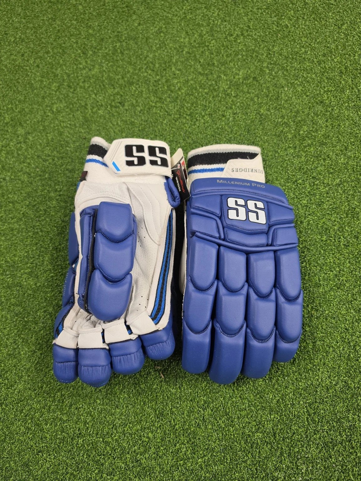 Flat top-down view of blue and white SS TON Millennium Pro adult cricket batting gloves resting on artificial turf