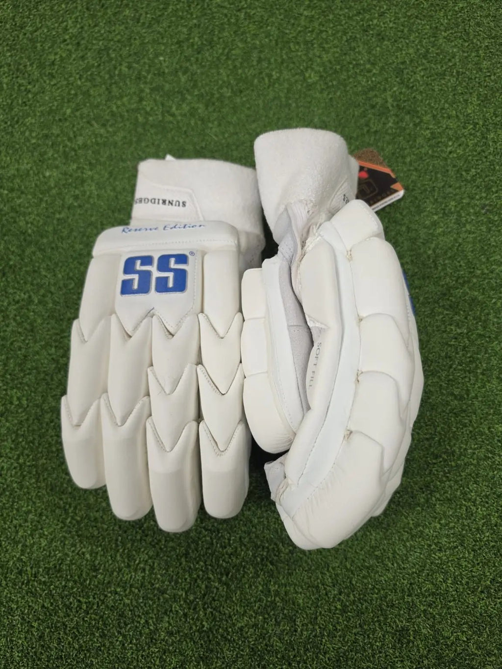 Pair of white SS Ton Reserve Edition cricket batting gloves showing front and side profile padding on green artificial turf