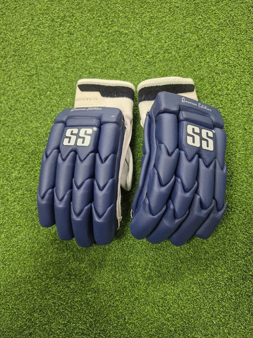 Pair of navy blue SS Ton Reserve Edition cricket batting gloves with white SS logos placed on artificial turf