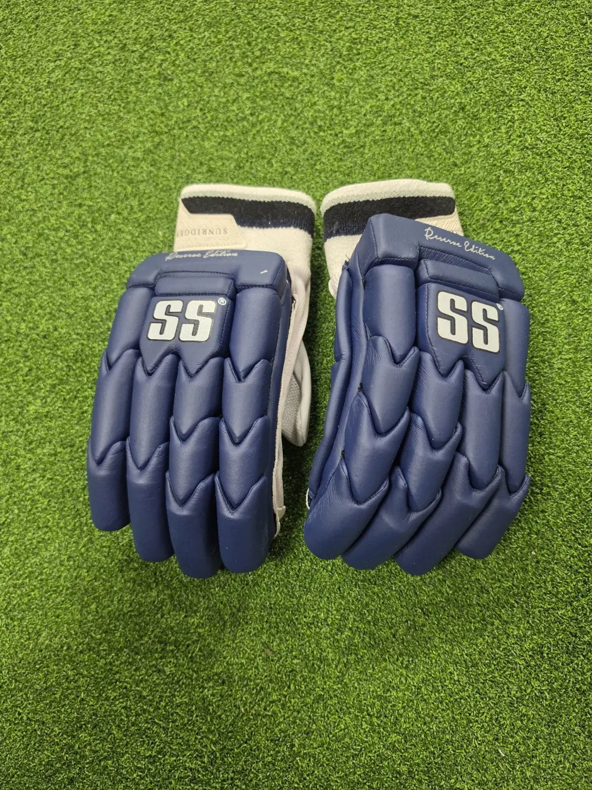 Pair of navy blue SS Ton Reserve Edition cricket batting gloves with white SS logos placed on artificial turf