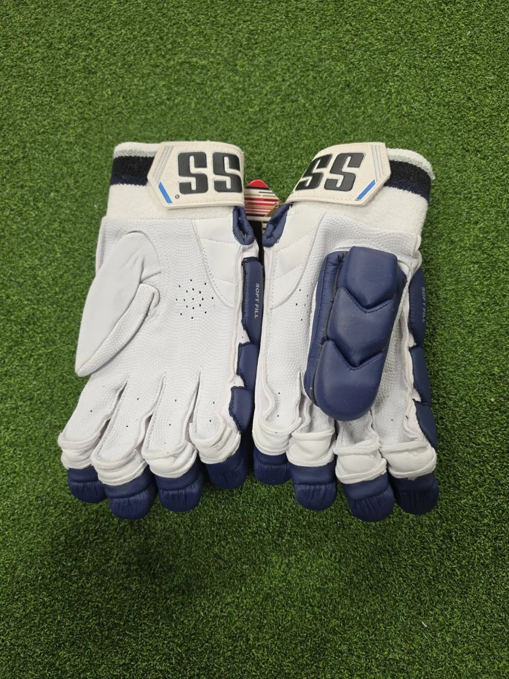 Palm view of navy blue SS Ton Reserve Edition cricket batting gloves showing leather grip, airflow perforations, and padded thumb protection on green turf