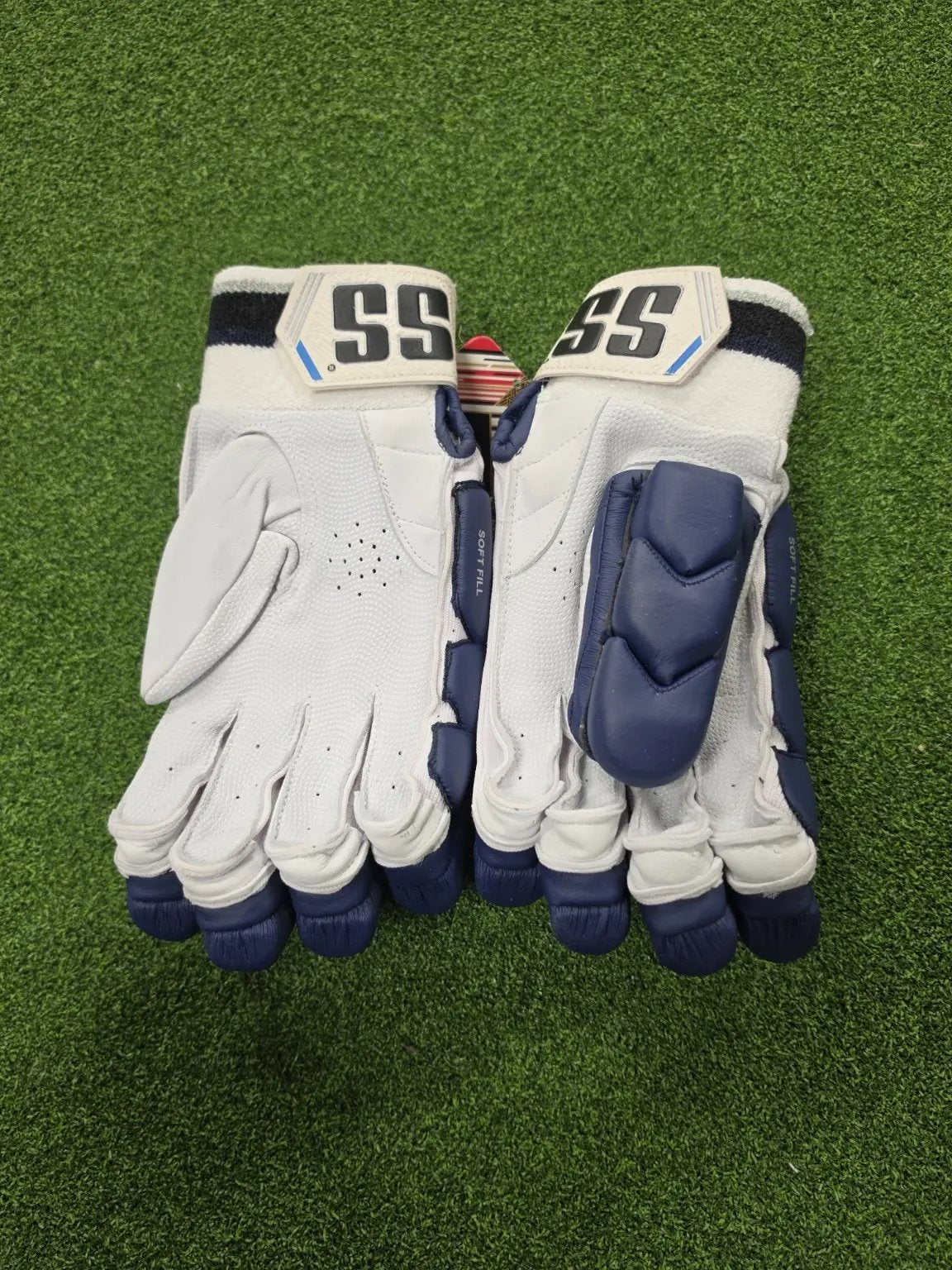 Palm view of navy blue SS Ton Reserve Edition cricket batting gloves showing leather grip, airflow perforations, and padded thumb protection on green turf