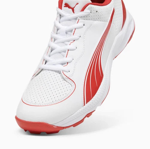Close-up view of the Puma 24 FH Rubber Cricket Shoe showing perforated white toe box, white laces, red Puma Formstrip, and red rubber outsole.