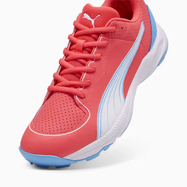 Close-up view of the Puma 24 FH Rubber Cricket Shoe in pinkish-red featuring a white Puma Formstrip with luminous blue trim and matching blue rubber outsole.