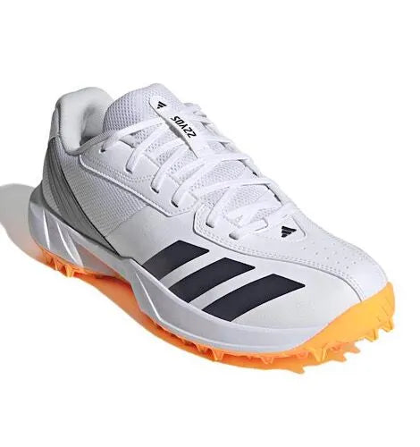 Front three-quarter angled view of the white Adidas 22YDS Spikeless Cricket Shoe highlighting the textured toe overlay and orange spiked outsole.