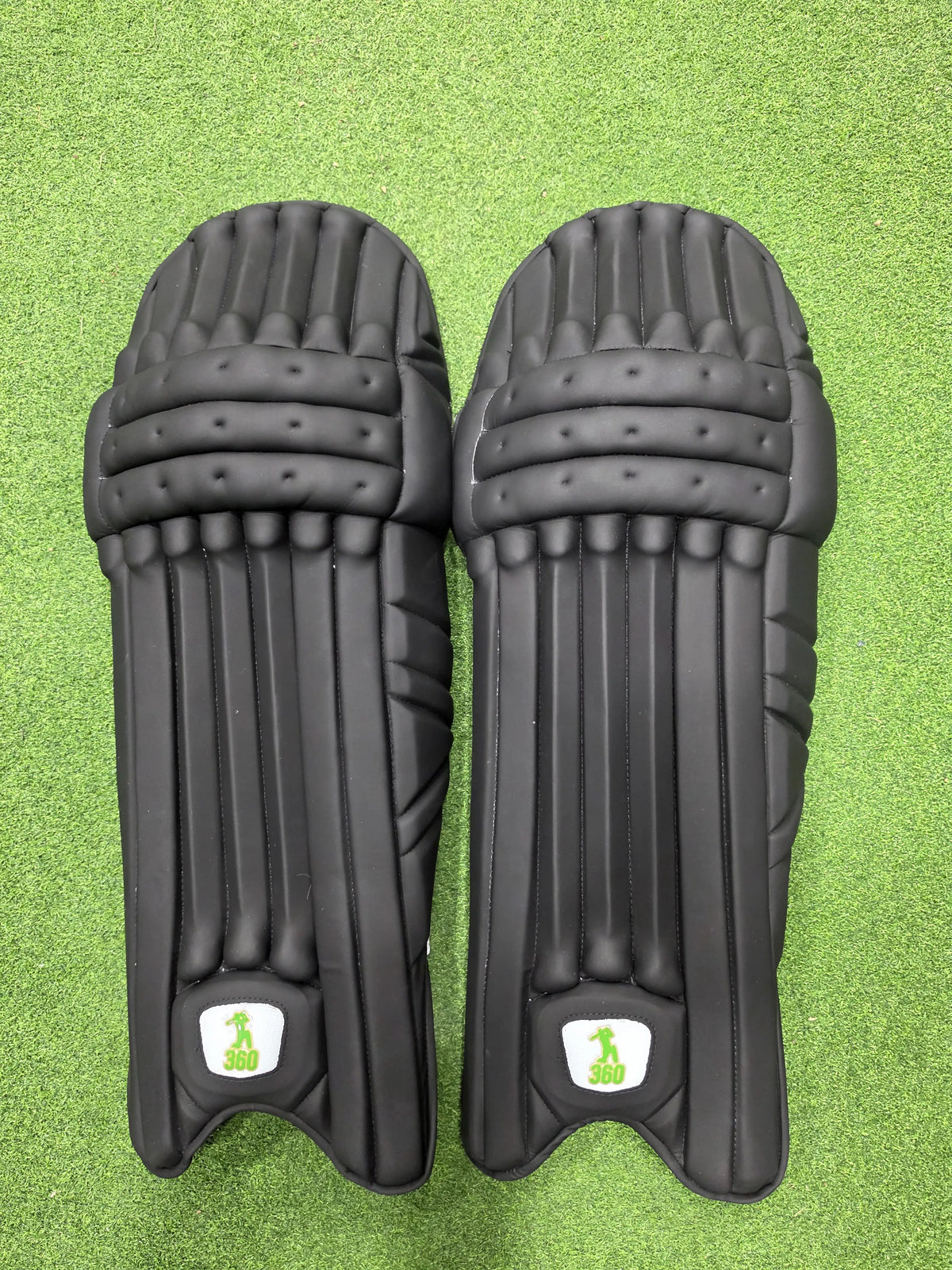 Front view of EM 360 Bull Ring black cricket batting pads on green artificial turf.