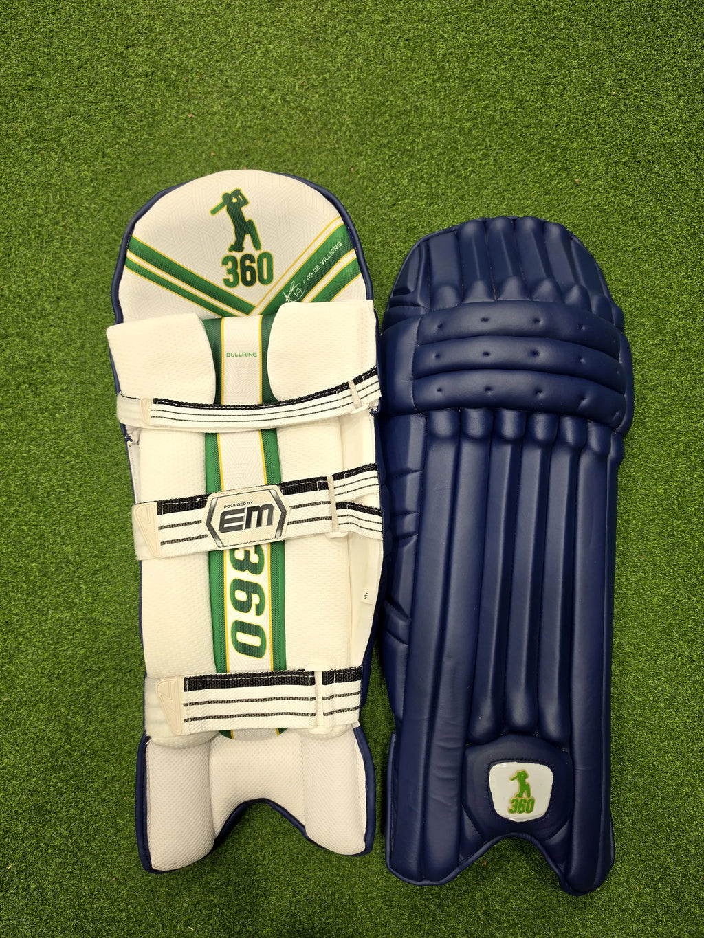 Front face and inner padded back view of EM 360 Bull Ring adult navy blue cricket batting pads on artificial grass on Alberta.