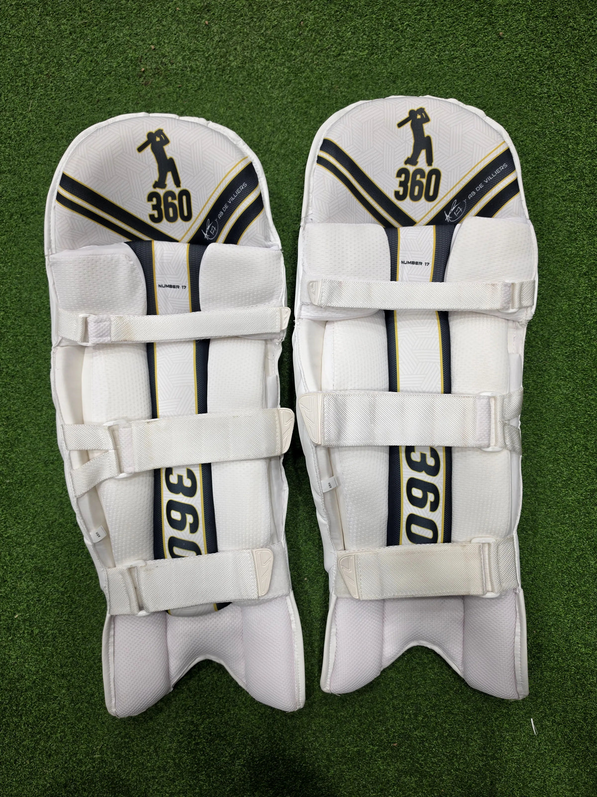 Inner padding and white straps of EM 360 No 17 cricket batting pads on green artificial turf.