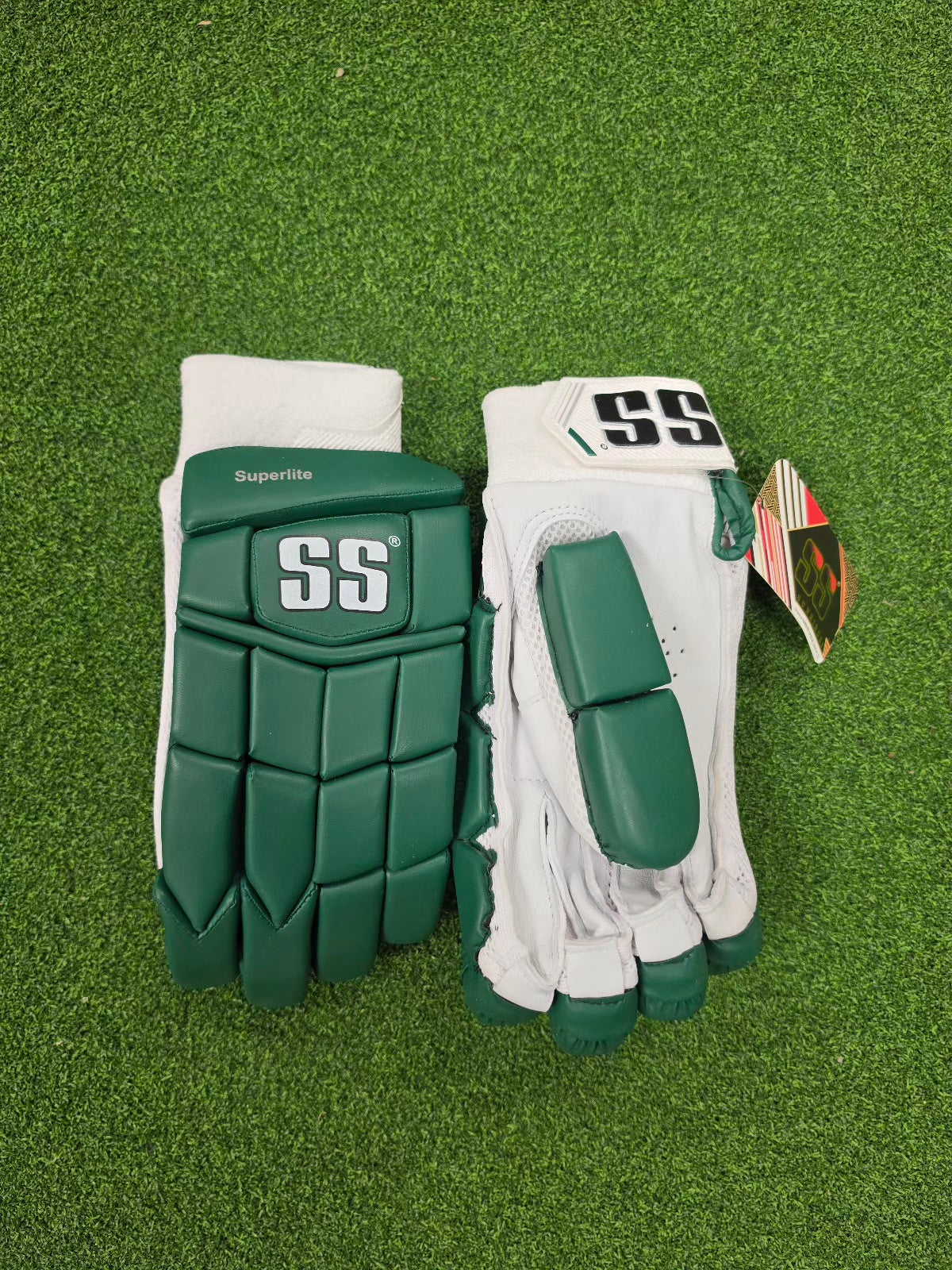 Green and white SS Superlite batting gloves showing the backhand and palm side by side on green turf.
