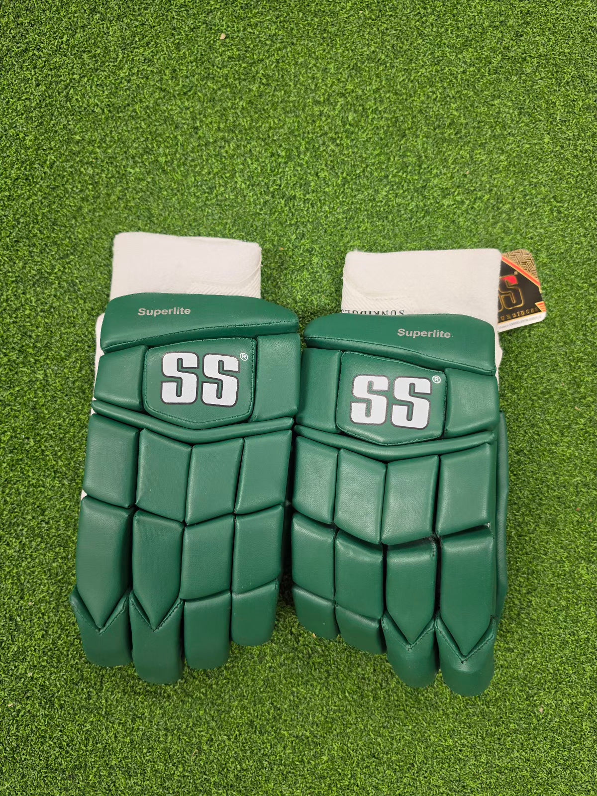 Backhand view of green SS Superlite batting gloves with white cuffs on green turf.