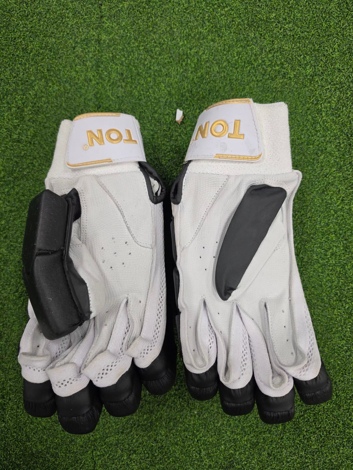 A pair of premium white and black SS Ton cricket batting gloves displayed on a green turf background at Alberta Cricket Store Canada.